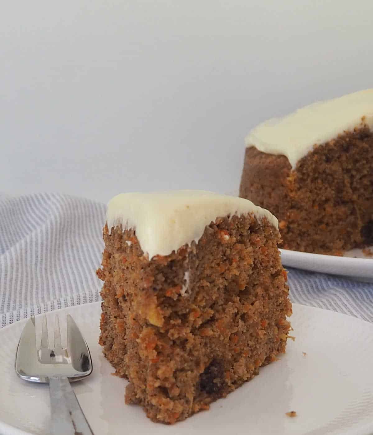 slice of Carrot Cake topped with cream cheese frosting sitting on a white plate.
