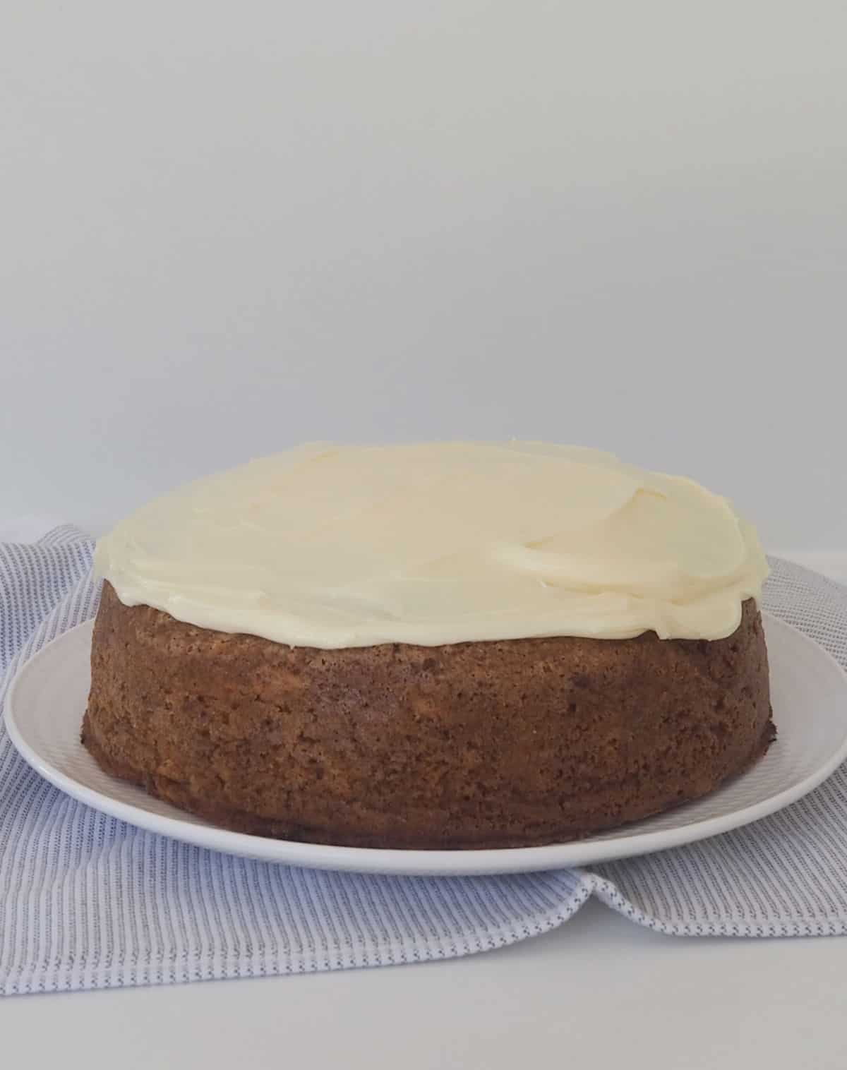 Carrot Cake topped with cream cheese frosting sitting on a white plate.