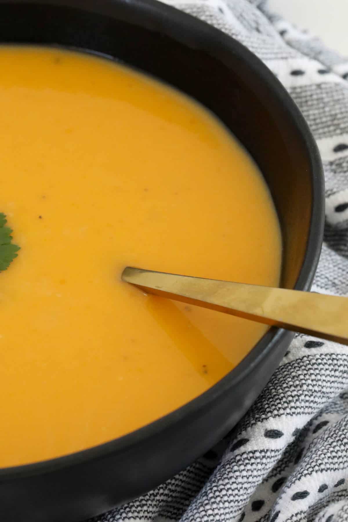 A gold spoon in a bowl of dairy free pumpkin soup.