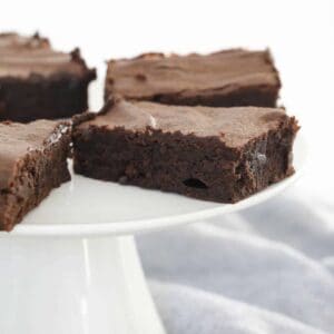 Slices of rich, chocolate brownies on a white cake stand.