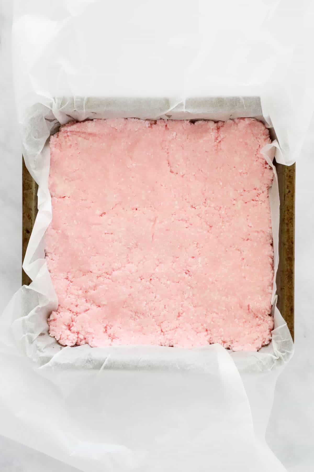 Pink coconut mixture pressed into a baking tin.