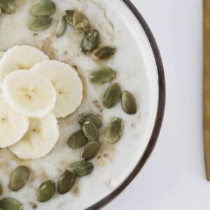 An overhead shot of cooked oats in a bowl with banana and seeds.