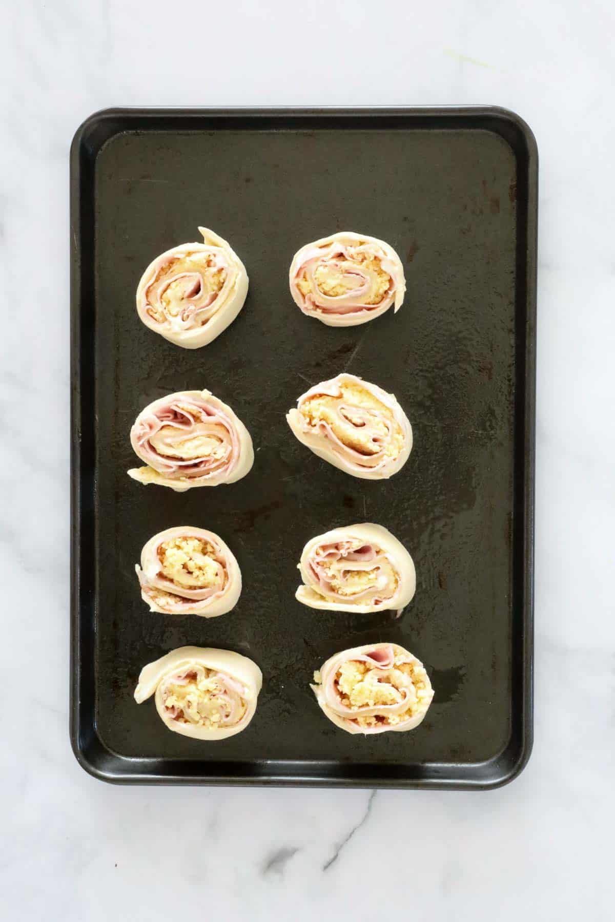 Ham and cheese scrolls on a baking tray.