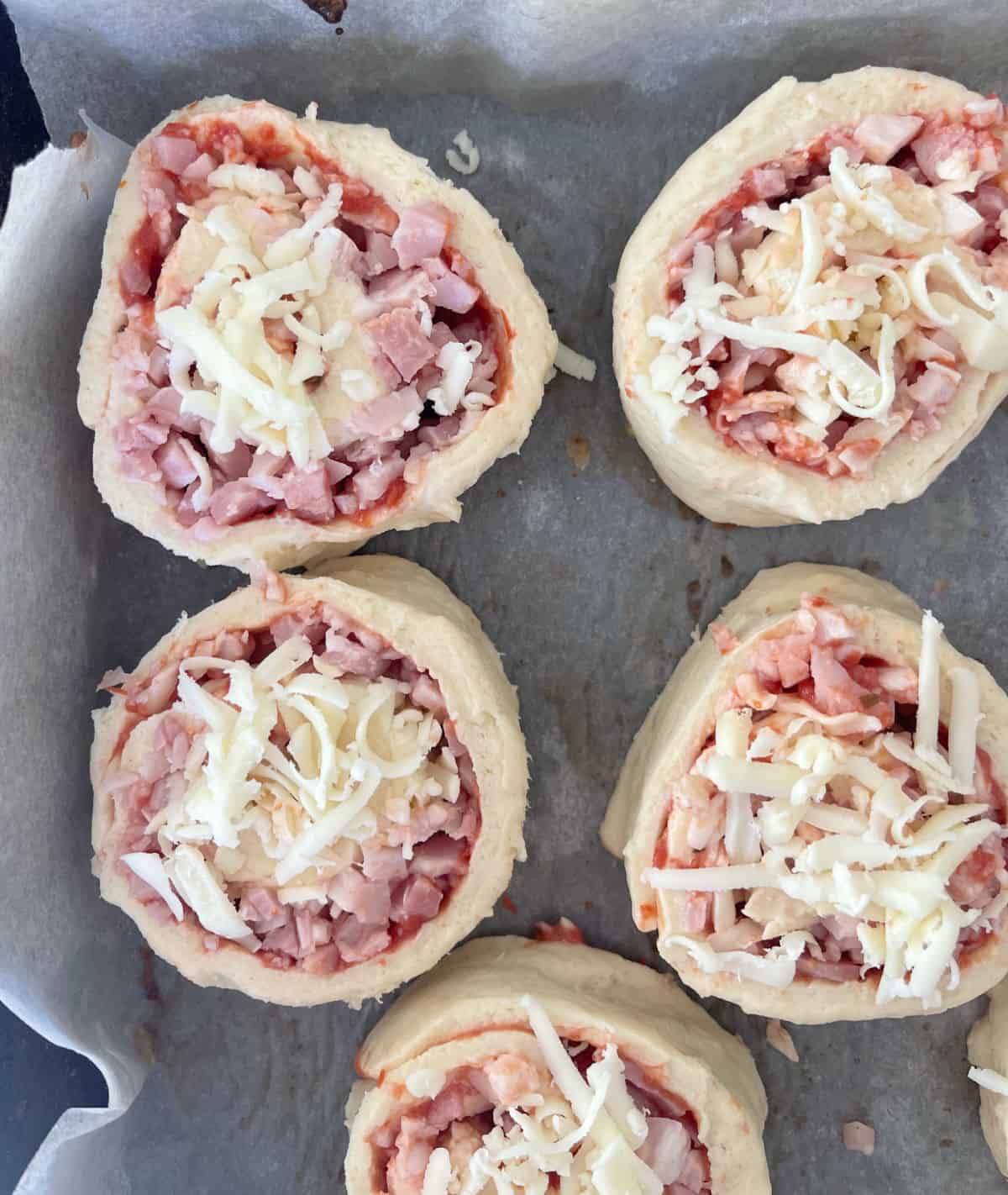 Uncooked Pizza Scrolls sitting on a lined baking tray.