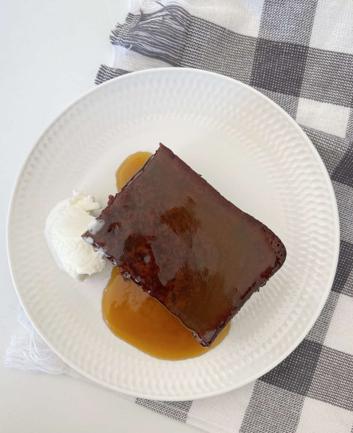A slice of sticky date pudding sitting on a white plate with caramel sauce and ice-cream.