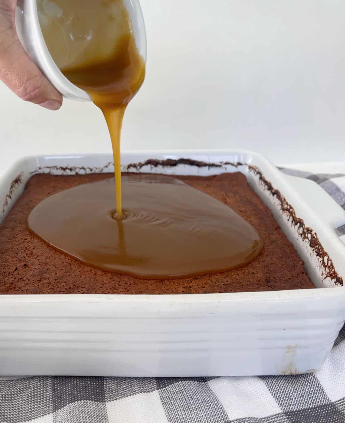 Caramel sauce being poured over the top of sticky date pudding.