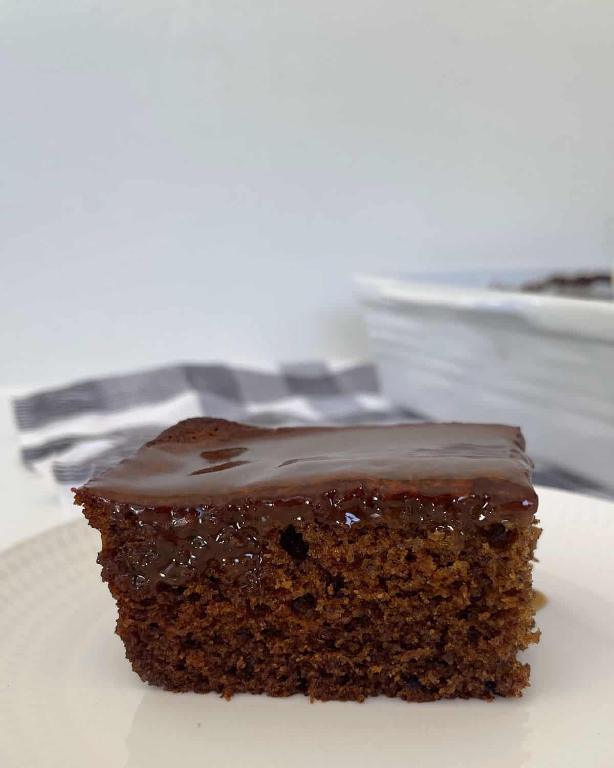 Side view of a slice of sticky date pudding on a white plate.