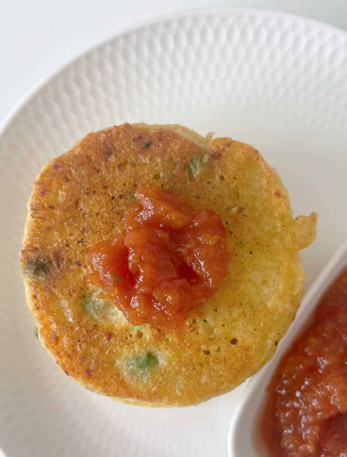 Overhead view of stack of vegetable fritters topped with tomato relish.