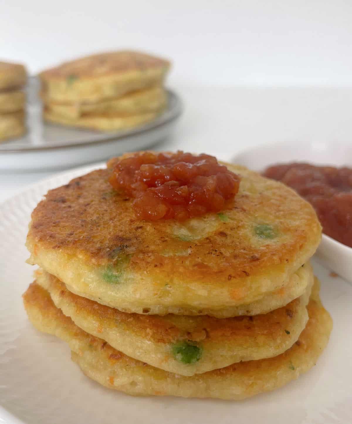 Three Vegetable fritters topped with tomato relish sitting on a white plate.