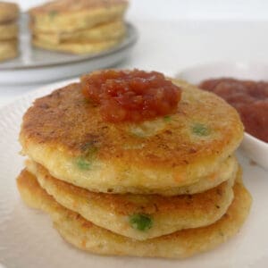 Three Vegetable fritters topped with tomato relish sitting on a white plate.