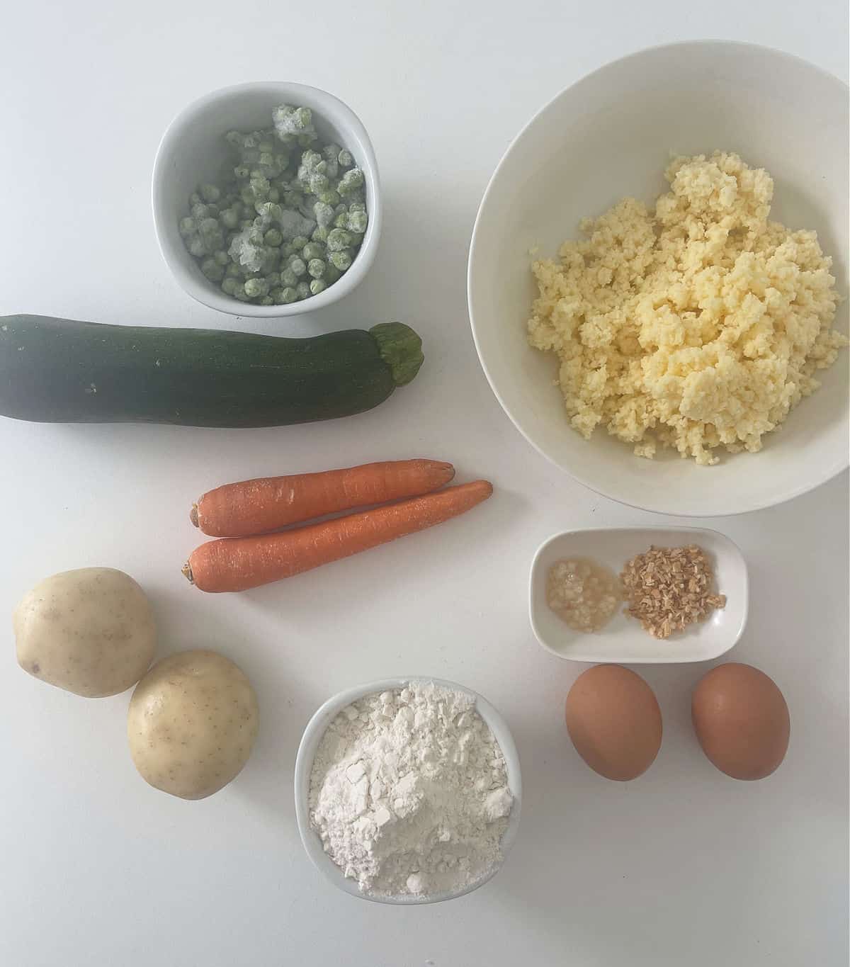 Ingredients to make vegetable fritters on a white bench top.
