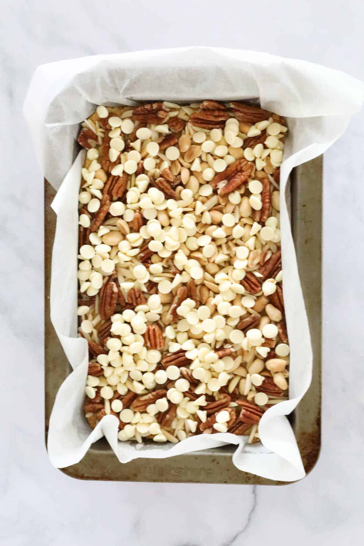 Nuts and white chocolate chips in a slice tin.