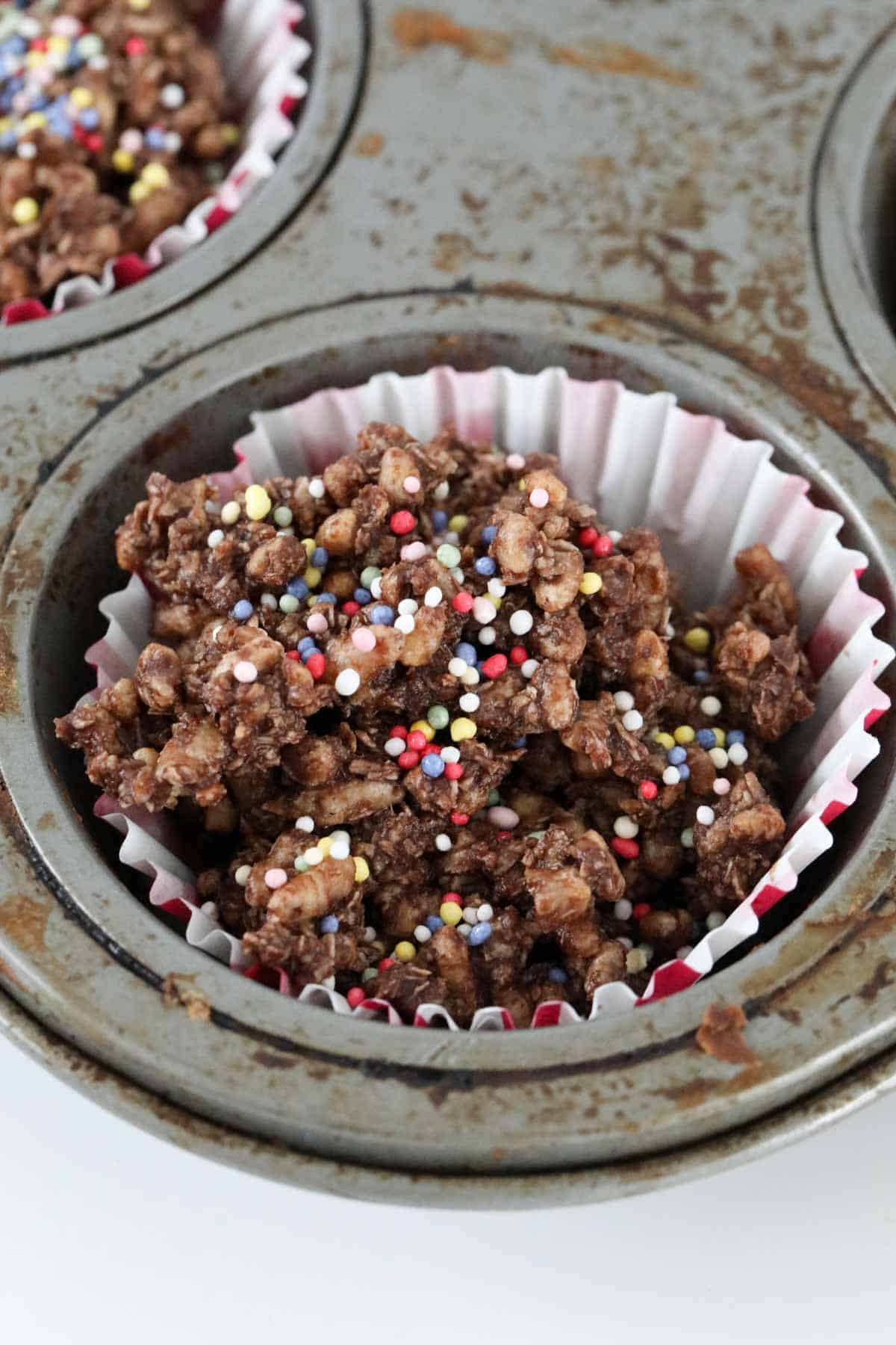 Sprinkles on top of chocolate crackles in a muffin tin.