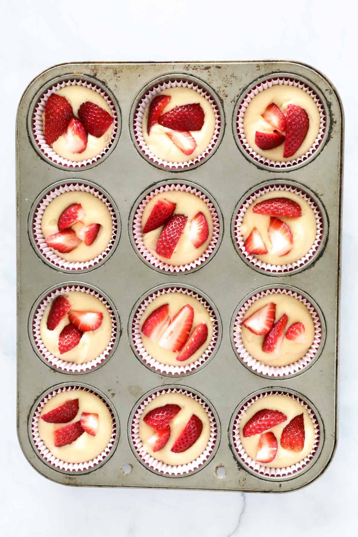 Strawberries in cupcake mixture in a muffin tin.