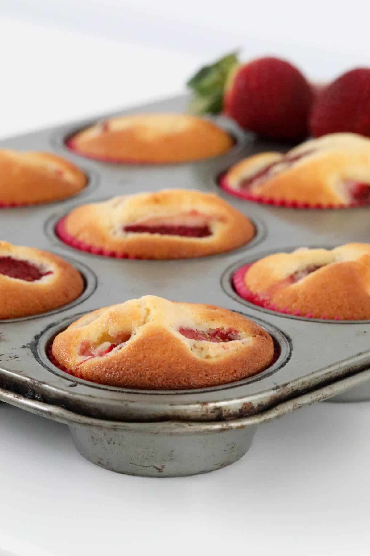 A baking tray filled with cupcakes with strawberries.