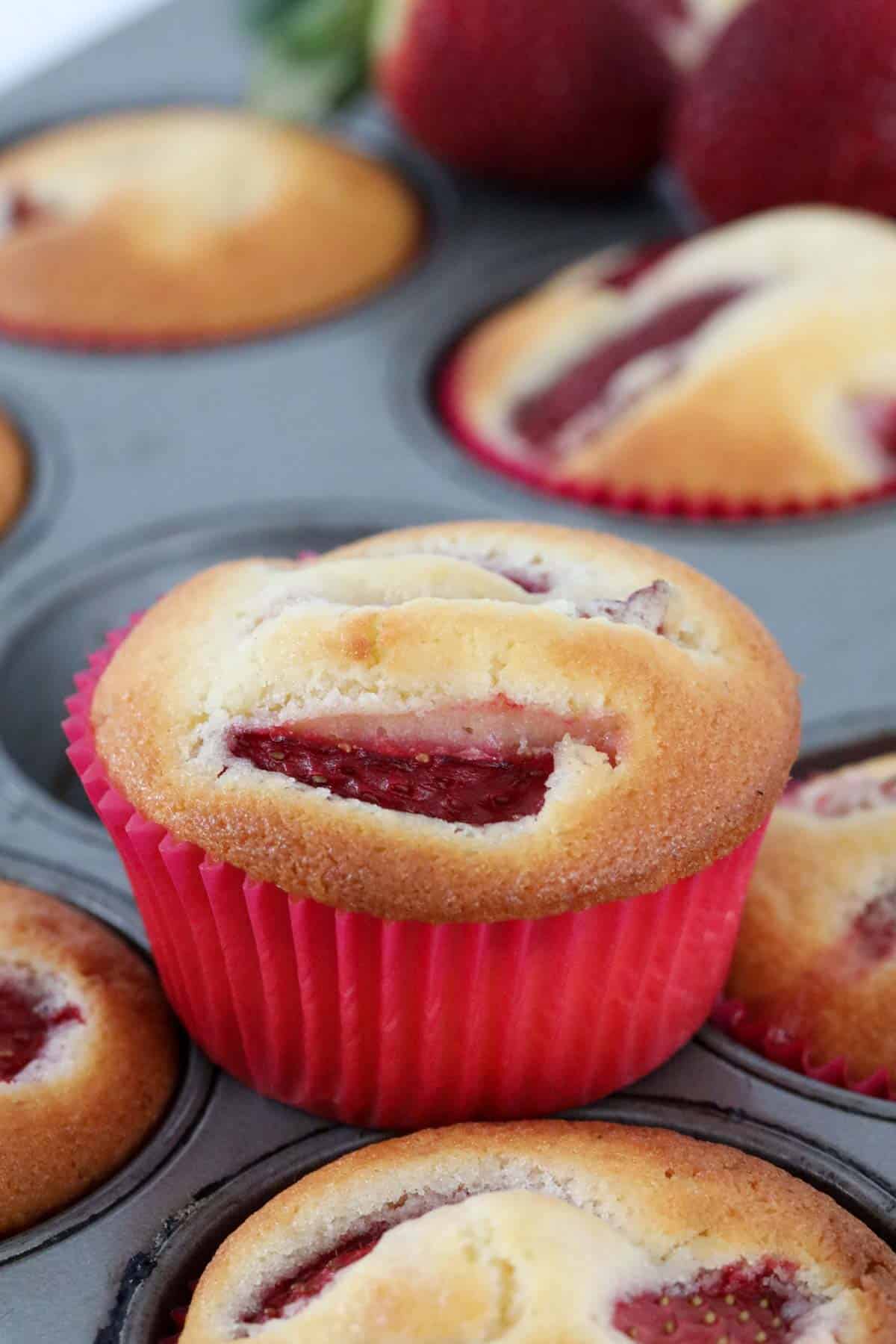 A strawberry cupcake on top of a muffin tray.