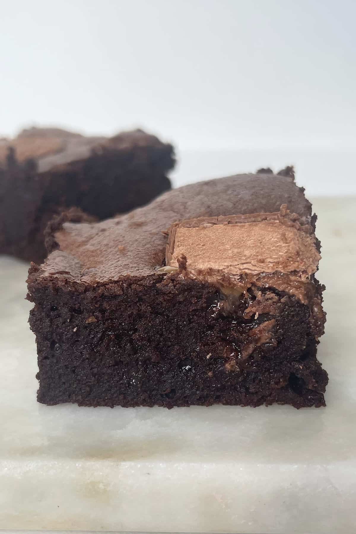 Side view of a mars bar brownie on a stone serving tray. In the background is another brownie.