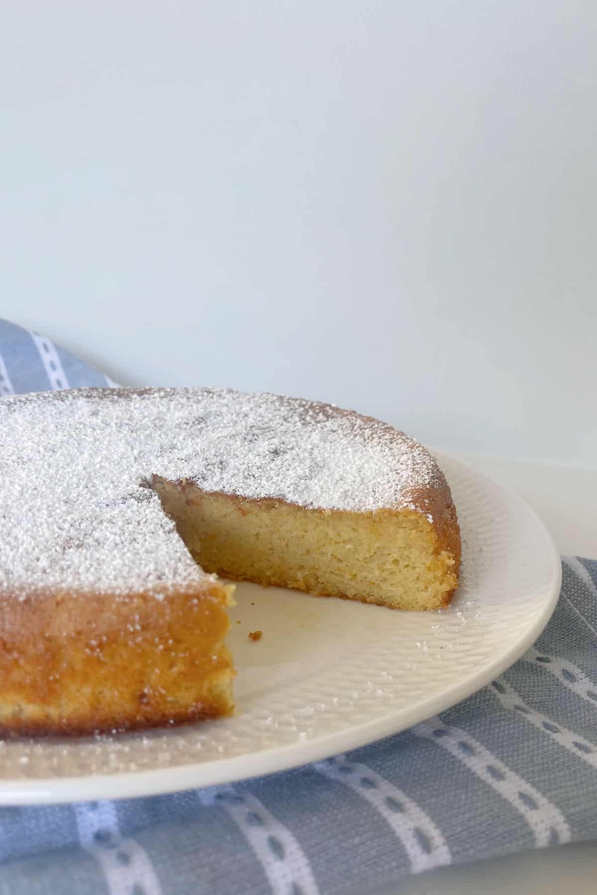 Whole Orange Cake dusted with icing sugar sitting on a white plate.