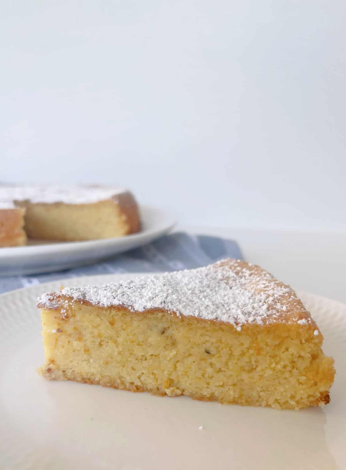 Slice of Whole Orange Cake dusted with icing sugar sitting on a white plate.