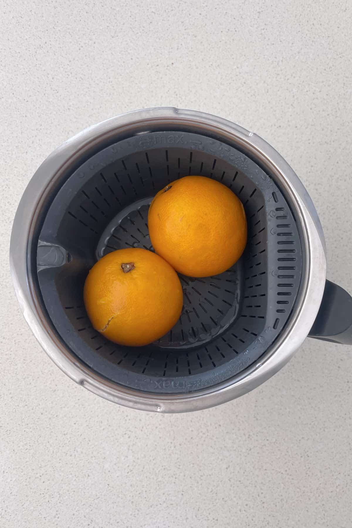 Two cooked oranges sitting in a steaming basked of a Thermomix.