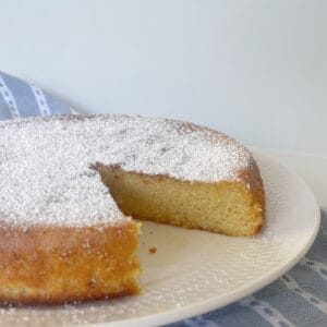 Whole Orange Cake dusted with icing sugar sitting on a white plate.
