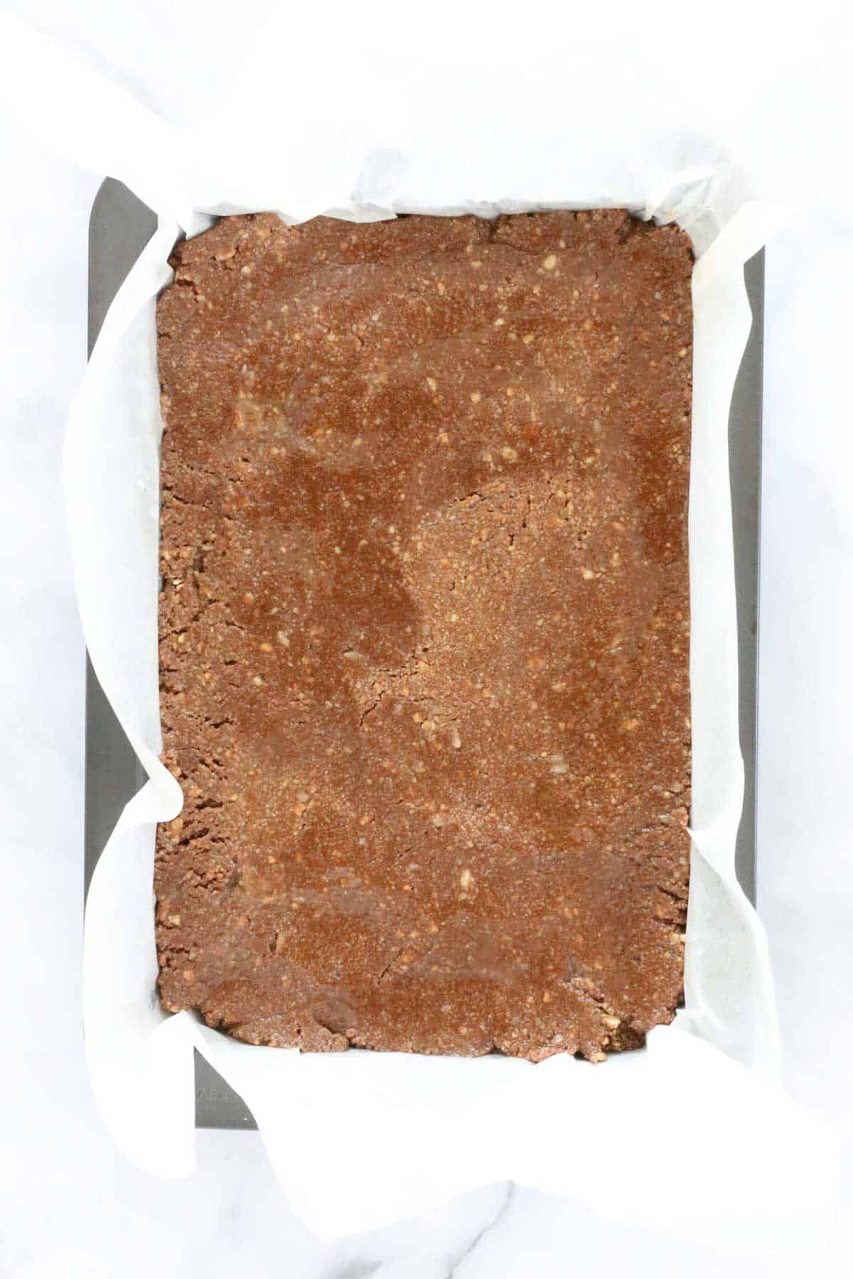 Chocolate slice mixture pressed into a tin.