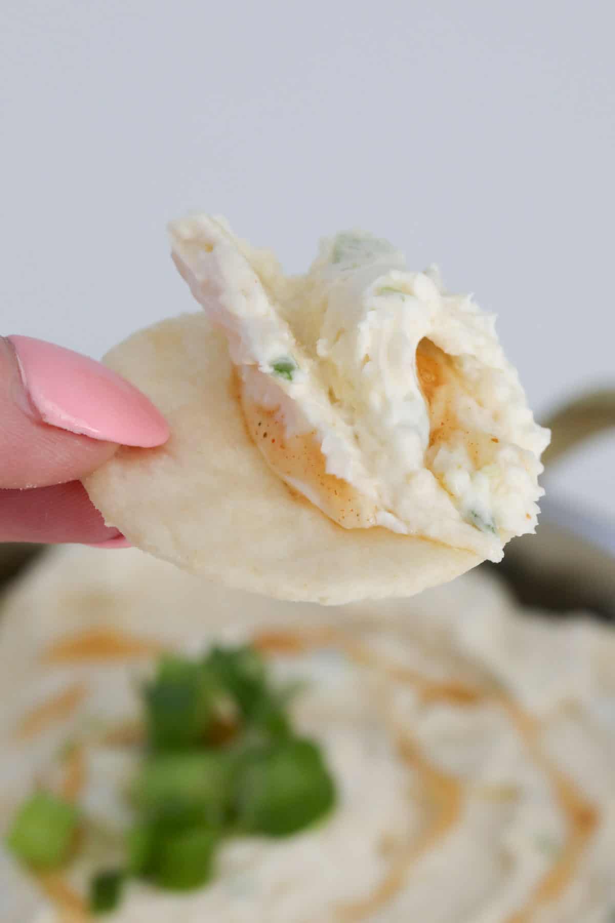 A hand holding a cracker with a creamy dip.