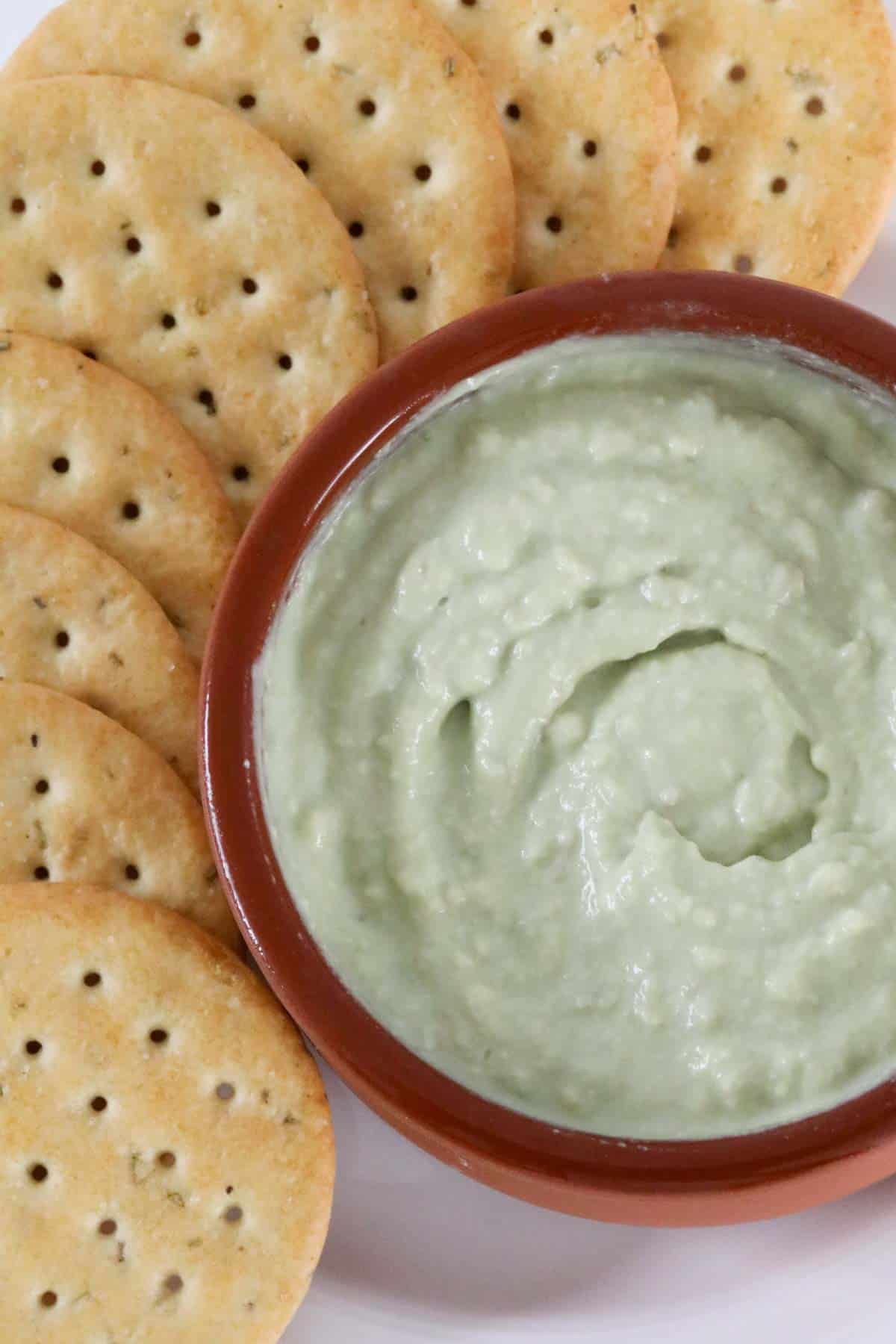 Crackers next to a creamy green dip.