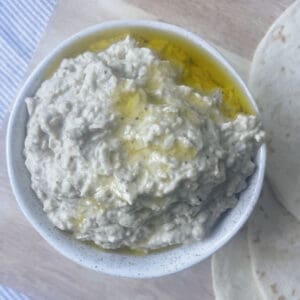 Baba Ghanoush drizzled with olive oil in a white speckled bowl sitting on chopping board.