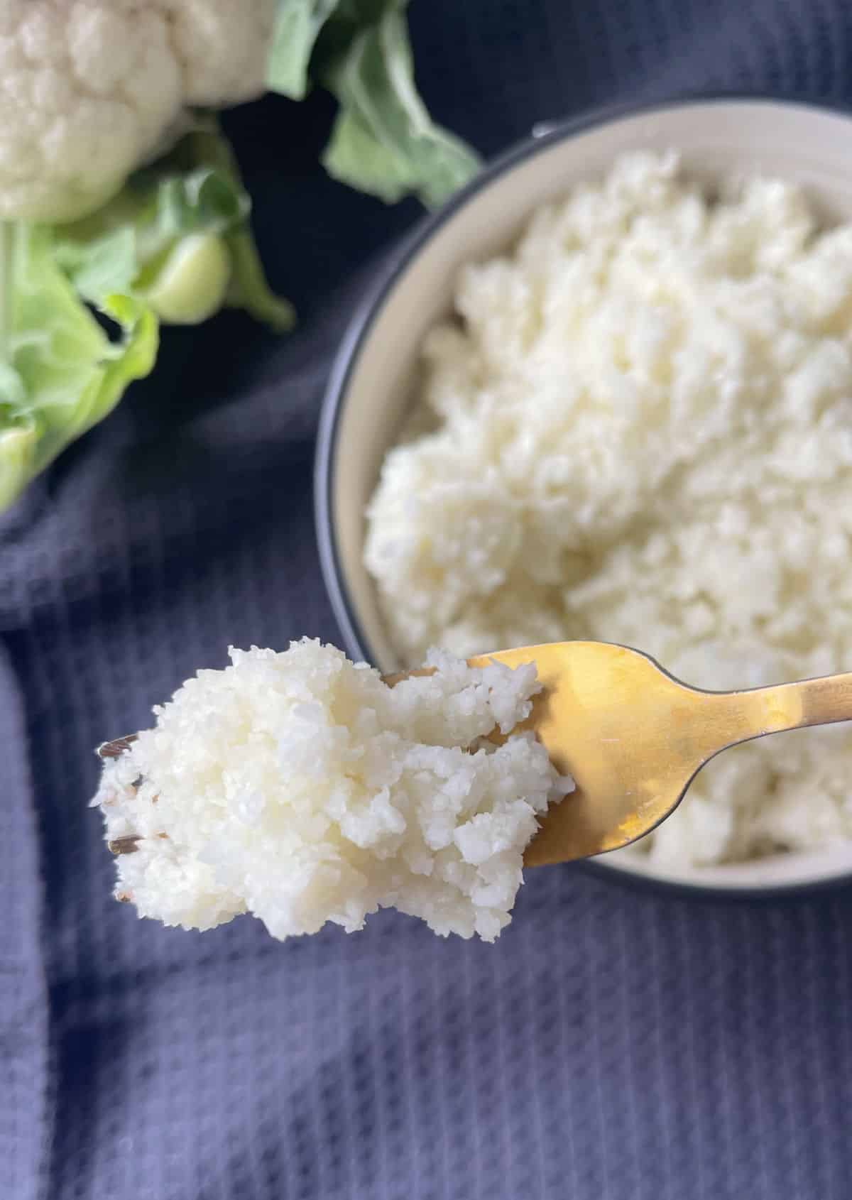 GOld fork scooping up cauliflower rice.