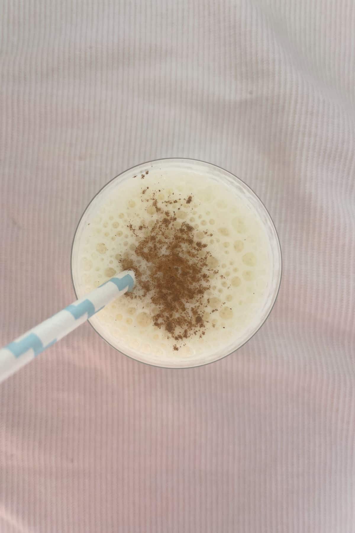 Overhead view of a banana smoothie sprinkled with cinnamon sitting on a pink towel.