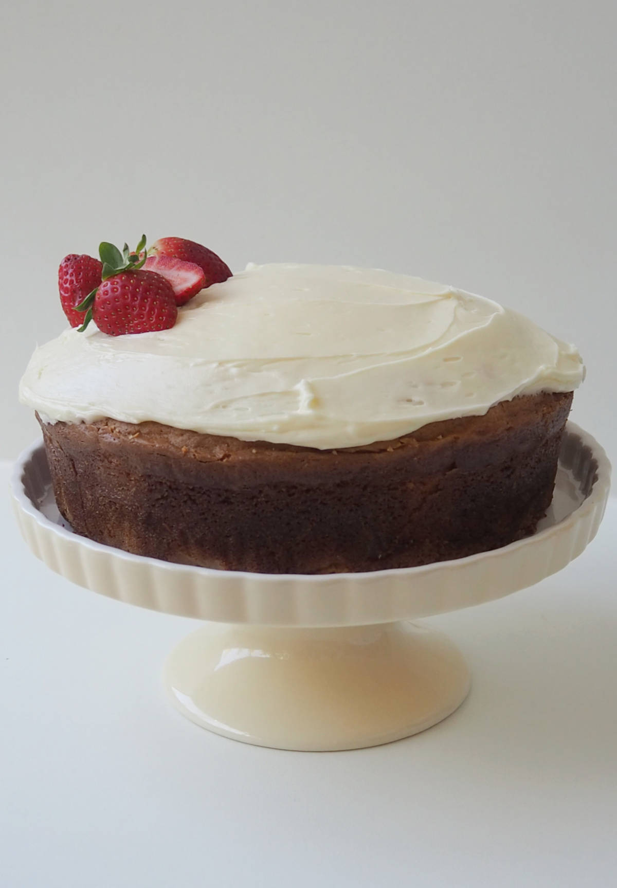 White chocolate mud cake topped with white chocolate ganache and strawberries on a cream cake platter.