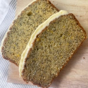 Overhead view of Lemon and Poppy Seed Cake Sliced and sitting on a pale timber serving board.