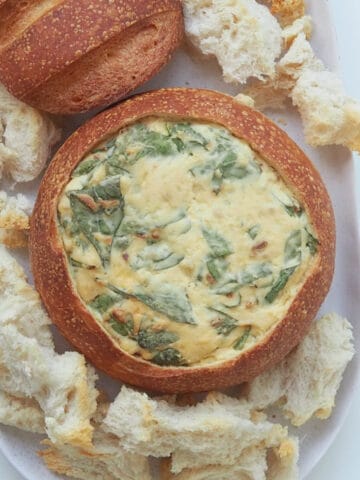 Overhead view of a spinach cob loaf on a white oval platter with toasted bread pieces around it.