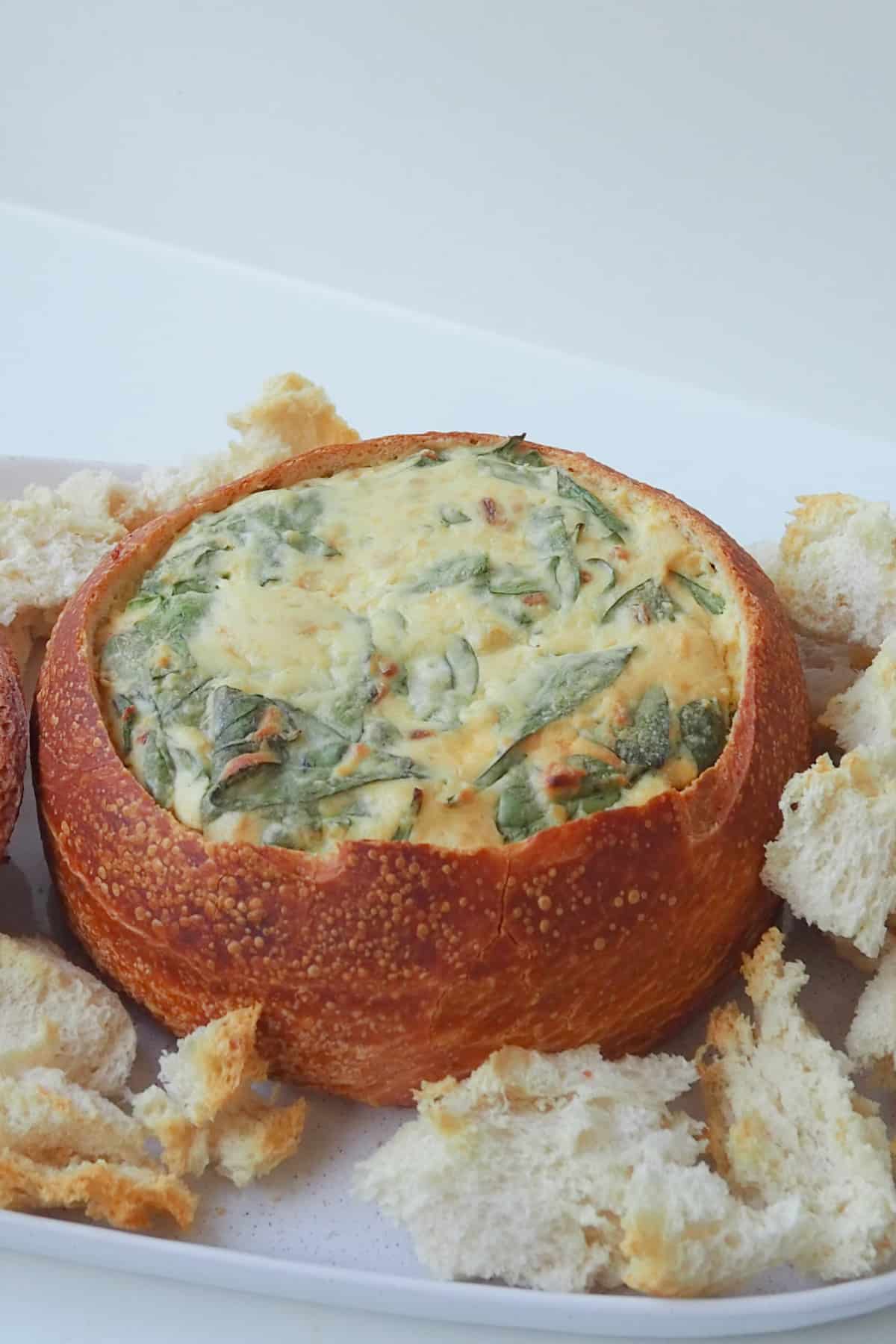 Side view of spinach cob loaf dip on a white platter with bread pieces around it.