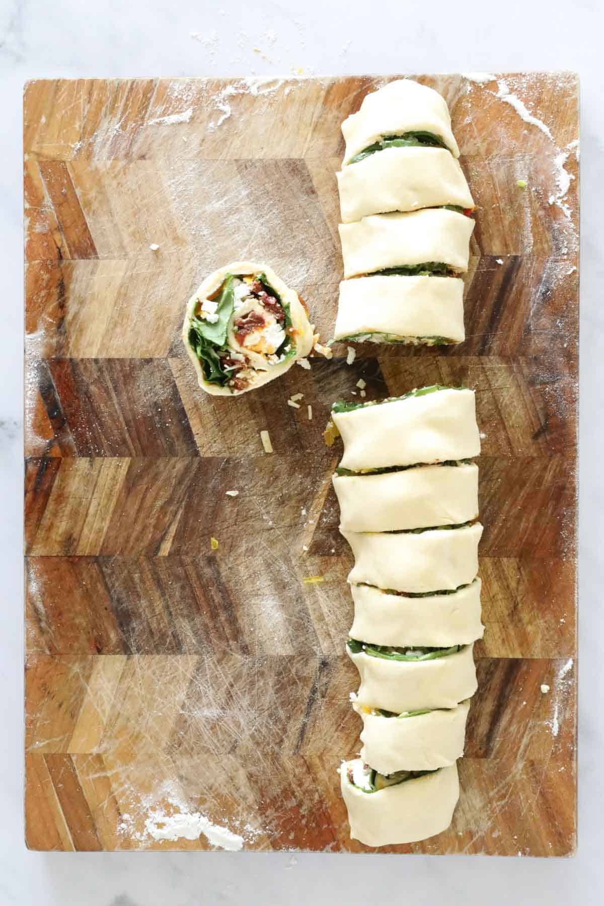 Pinwheel scroll with spinach being cut on a board.