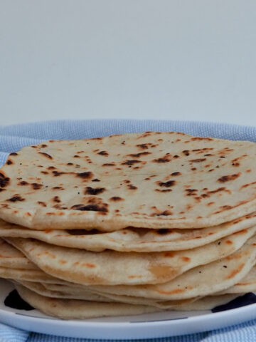 Stack of 10 tortillas sitting on a blue and white spotted plate.