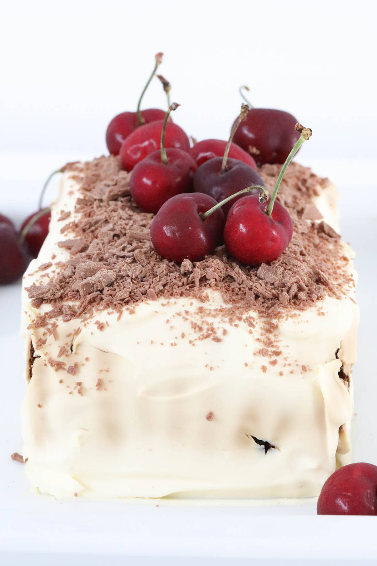Cherries and chocolate on top of a cream covered dessert.