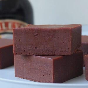 Two pieces of Baileys Fudge sitting on a white serving stand with a bottle of Baileys in the background.
