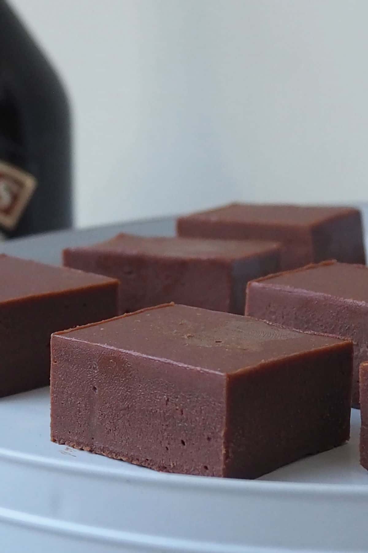 Slices of Baileys Fudge sitting on a white serving stand with a bottle of Baileys in the background.