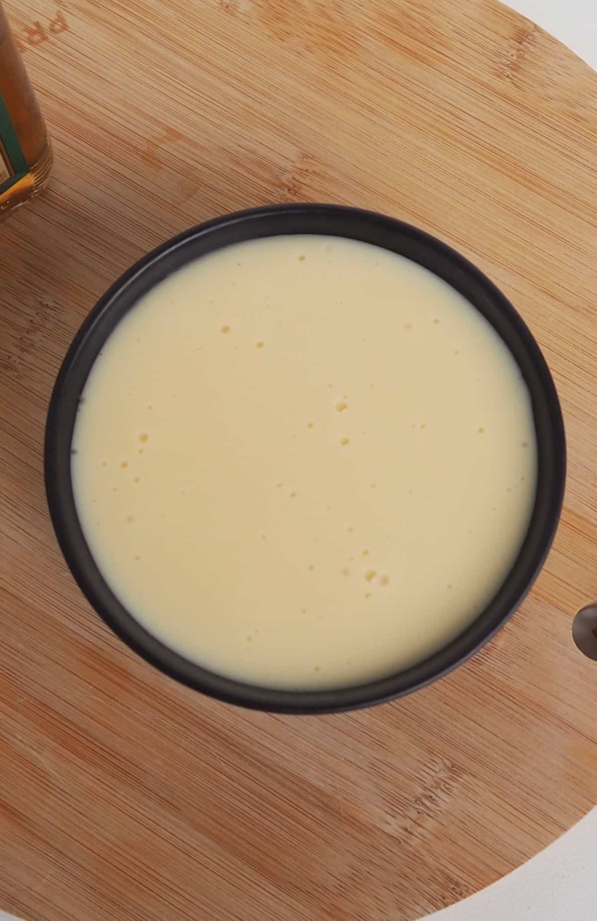 Overhead view of Brandy Custard in a black bowl sitting on a wooden board.