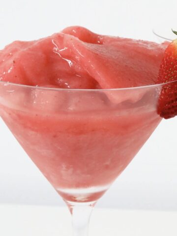 A strawberry on the side of a pink frozen cocktail.