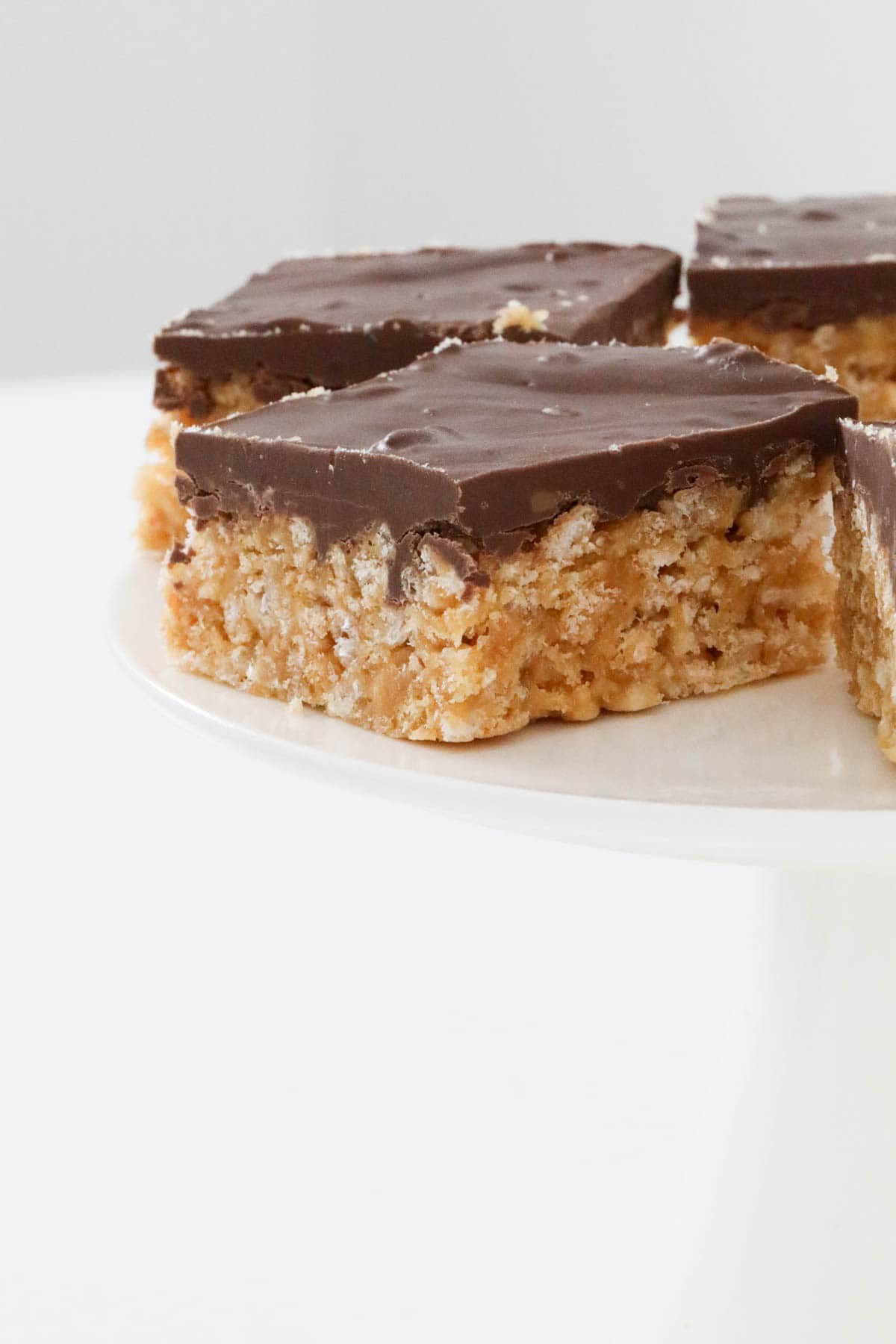 A cake stand with peanut butter slice with chocolate on top.