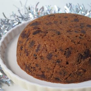 Close up Side view of a Christmas Pudding on a cream cake stand. in the background is silver tinsel.