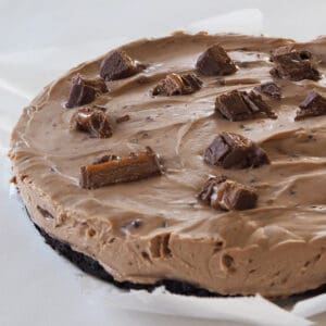 Side view of a Mars Bar Cheesecake sitting on a sheet of baking paper.