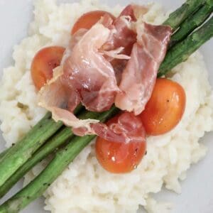 An overhead shot of fresh vegetables and prosciutto on top of a creamy risotto.