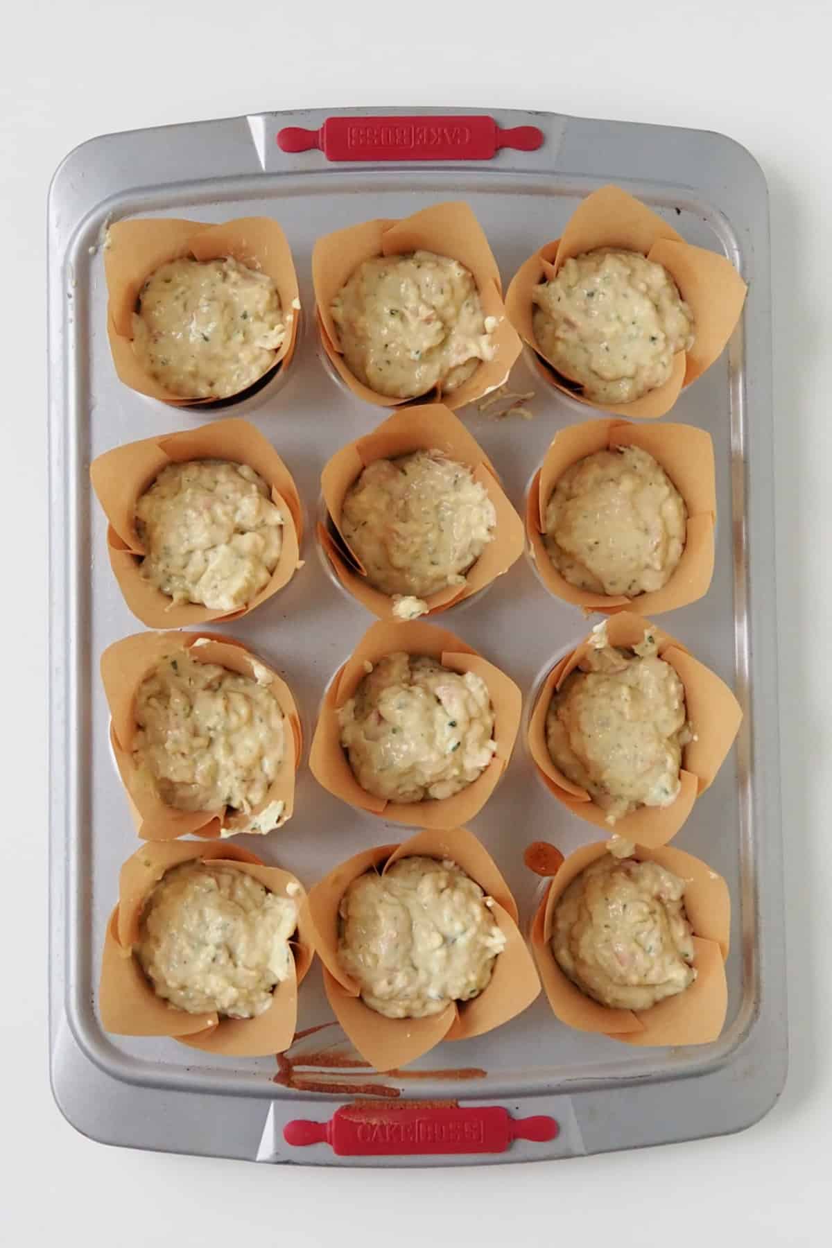 Savoury muffin mixture in paper cases in a muffin tray ready to go into the oven.