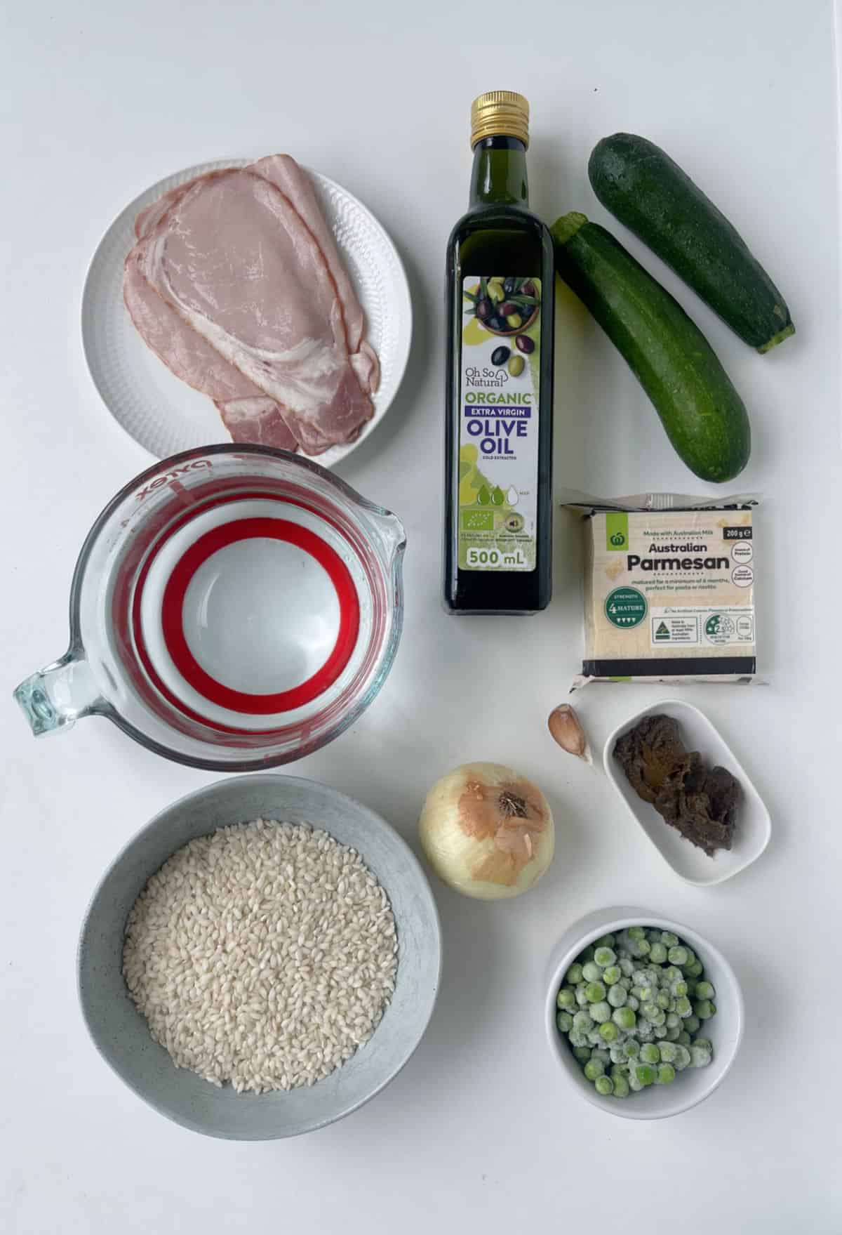 Ingredients to make Zucchini, Pea and Bacon Risotto on a white bench top.