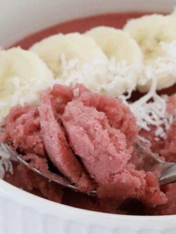 A spoon scooping from a berry acai bowl topped with banana and coconut.