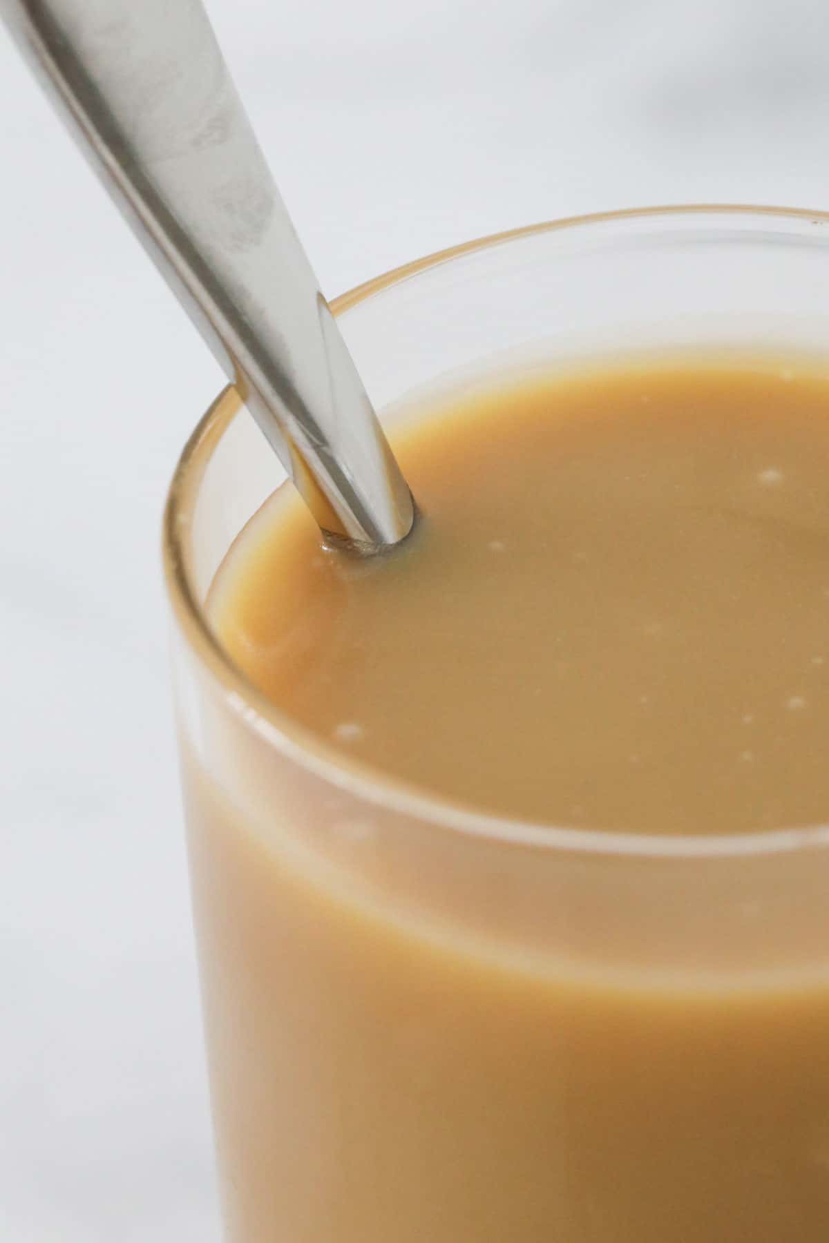 A spoon in a glass jar of caramel sauce.